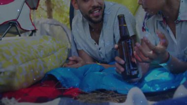 Kamp çadırında bira içen ve uyku tulumunda sohbet eden bir çift. Macera, açık hava, samimiyet, rahatlama, kırsal, bağlantı, doğa