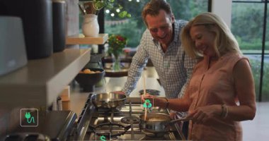 Gaz tenceresinde sos karıştıran yaşlı çift yemek takımlarının etrafında enerji verimliliği simgeleri sergiliyor. Son sınıf, çift, mutfak, yemek pişirme, modern, enerji, sürdürülebilirlik