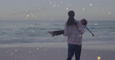 Anne kızını alacakaranlıktaki sahilde kaldırıyor. Neşeli sağlık bağları etrafında dönen parlayan ışıklar yakıyor. Aile, açık hava, günbatımı, bağlantı, dinginlik, rahatlık, portre