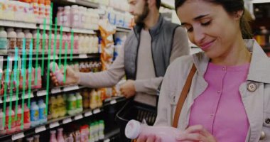 Kadın mağaza koridorundaki pembe içeceğe uzanıyor ve erkekler meyve suyu etiketlerini karşılaştırırken beslenme etiketini okuyor. Perakende, alışveriş, yaşam tarzı, canlı, renkli, sağlık, ferahlatıcı