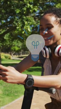 Akıllı telefon kullanan Afro-Amerikan bir kadının üzerindeki ampul ikonlarının animasyonu. Dijital olarak oluşturulan küresel sosyal medya, ağlar, dijital arayüz ve veri işleme kavramı.