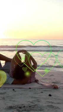 Yaz aylarında kumsalda yatan birbirine aşık çift üzerinde hareket eden kalplerin animasyonu. Aşk, romantizm, Sevgililer Günü ve tatil konsepti dijital olarak oluşturulmuş video.