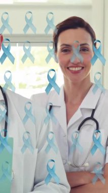 Kadın ve erkek doktorlardan oluşan gülümseyen bir ekiple mavi kanser kurdelelerinin animasyonu. Kanser pozitif farkındalık kampanyası, tıbbi ve sağlık hizmetleri konsepti dijital olarak oluşturulmuş video.