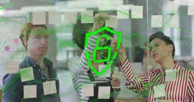 Meslektaşlar cam panoya notlar ekleyerek güvenlik kalkanı ve kilit simgesini şekillendiren yeşil hattı başlatıyorlar. İşbirliği, beyin fırtınası, dijital arayüz, güvenlik, takım çalışması, yenilik, ofis