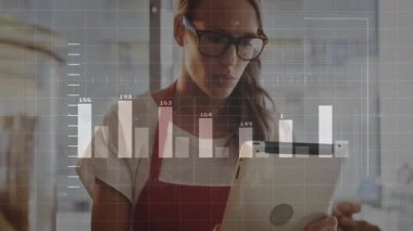 Yetişkin bir kadın elinde tablet tutarak kafede hareketli çizelgelerle dükkan ölçümlerini gözden geçiriyor. Analizler, iş dünyası, veri, teknoloji, perakende, profesyonel, modern