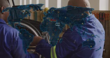 Tekerlekli sandalyeyi tamirat atölyesinde tamir ederken harita soluklaşıyor, matkap cıvatası deliniyor. Teknisyenler, işbirliği, sanayi, kesinlik, yenilik, mühendislik, takım çalışması