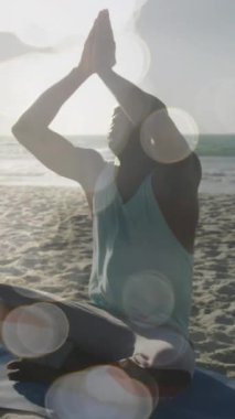 Sahilde yoga meditasyonu yapan Afro-Amerikan bir adam üzerinde parlayan ışıkların animasyonu. Küresel bağlantılar, refah, zindelik ve dijital olarak üretilen sağlıklı yaşam tarzı konsepti.