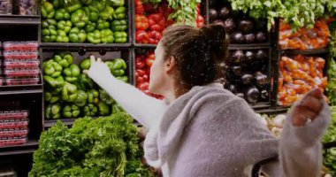 Alışverişçi, tazeliği incelerken öne eğilip markette yeşil dolmalık biber seçiyor. Üretim, market, alışveriş, sağlıklı, taze, yaşam tarzı, organik