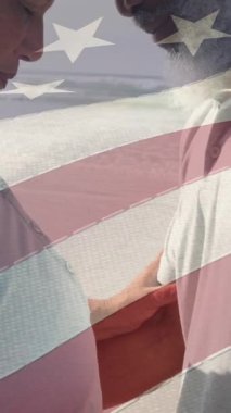 Amerika bayrağının animasyonu kumsalda birbirini kucaklayan mutlu yaşlı çiftin üzerinde. Amerikan vatanseverliği, milliyeti, yaz ve çeşitlilik konsepti dijital olarak oluşturulmuş video.
