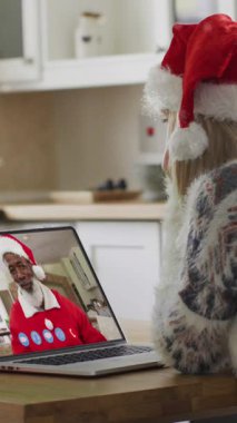 Dizüstü bilgisayardaki görüntülerde Noel Baba şapkalı mutlu beyaz kadının üzerine yağan kar animasyonu. Noel, gelenek ve kutlama konsepti dijital olarak oluşturuldu.