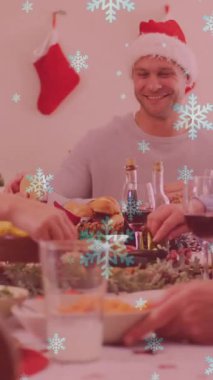 Gülen beyaz bir ailenin üzerine düşen kar animasyonu. Noel Baba şapkalarıyla yemek yiyorlar. Noel, kış, gelenek ve kutlama konsepti dijital olarak oluşturulmuş video.