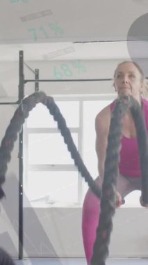 Beyazlı bir kadının spor salonundaki savaş halatlarıyla çapraz eğitimle ilgili arayüzdeki verilerin animasyonu. Fitness, egzersiz, güç, veri, dijital arayüz ve dijital olarak üretilen video.