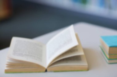Düz tasarım açık karton kapaklı kitap renkli kitap yığınları ve bulanık kitap raflarıyla masanın üstünde duruyor. Edebiyat, eğitim, bilgi, okuma, öğrenme, ilham