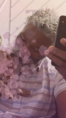 Animation of falling hearts over african american senior man using smartphone. International day of older persons concept digitally generated video.
