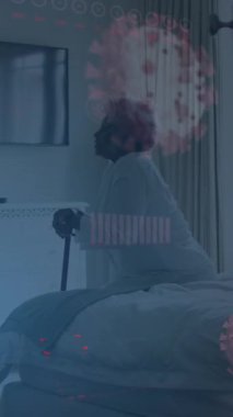 Animation of covid-19 data processing over sick african american senior woman sitting on bed. Covid-19 pandemic concept