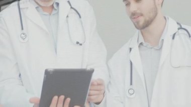Genç tıp doktoru tableti işaret ederek klinik inceleme taraması için yaşlılara eğilim veriyor. İşbirliği, teknoloji, sağlık, profesyonellik, teşhis, takım çalışması, modern