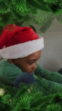 Noel Baba şapkası takan Afrikalı Amerikalı bir çocuk için köknar ağacı ve kar taneleri animasyonu. Noel, gelenek ve kutlama konsepti dijital olarak oluşturuldu.