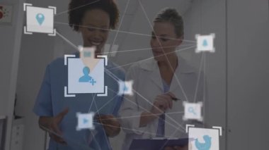 Hemşire ve doktor hastane koridorunda yürürken hasta dosyalarını inceliyor, ikonları aktifleştiriyor. Tıbbi personel, işbirliği, dijital sağlık, klinik takım çalışması, sağlık teknolojisi, hastane ortamı, profesyonel diyalog