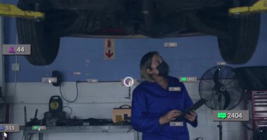 Otomotiv teknisyenleri araba kaldırma işleminin altında kaydırma tabletleri ile çarpma ölçümlerini görüyorlar. Mekanik, dijital, endüstriyel, teknoloji, ilerleme, yenilik, bakım