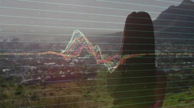 Kadın tepenin yamacında kollarını açıyor ve dalga formu grafiklerini başlatıyor. Şehir vadisinde verileri görselleştiriyor. Açık hava, fitness, zindelik, teknoloji, yenilik, sükunet, manzara