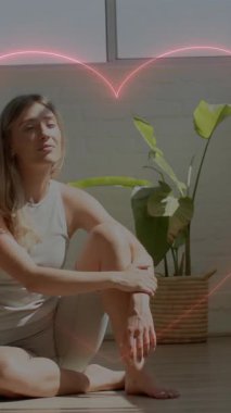 Yoga minderiyle yerde oturan, kalp animasyonuyla çevrili bir kadın. Sağlık, meditasyon, egzersiz, rahatlama, sağlık, spor