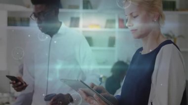 Adam telefonu kaydırıyor ve kadın tableti dinleyip teknik ekip çalışması için yüzen veri grafiklerini çalıştırıyor. İşbirliği, teknoloji, yenilik, dijital, modern, iletişim, çalışma alanı