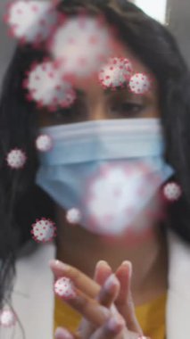 Ofiste yüz maskesi takan kadın portresinin üzerinde yüzen Coperid 19 hücrenin animasyonu. Coronavirus covid 19 salgını sırasında sağlık ve koruma dijital olarak üretilen video.