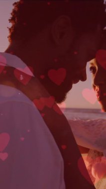 Afro-Amerikan yeni evli çifte karşı yüzen kırmızı kalpler sahilde birbirlerine sarılıyorlar. düğün ve aşk ilişkisi kavramı