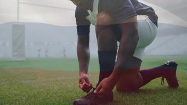 Oyuncu diz çökerken krampon bağlama hareketini başlatırken takım arkadaşı spor antrenmanı için arkadan geçiyor. Sporcu, takım çalışması, spor, fitness, hazırlık, eğitim, kararlılık