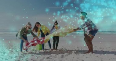 Dört kadın seyyar pazarlama için kareli battaniye ve sarı havluyu sallayarak kumsal kurulumuna başlıyor. Açık hava, boş zaman, takım çalışması, gündelik, canlı, arkadaşlık, yaşam tarzı