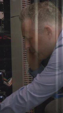 Caucasian senior male engineer talking on smartphone while working in computer server room. Cyber security and business data storage technology concept