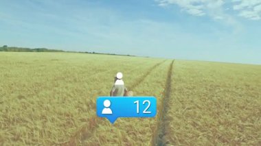 Adam buğday yolunda yürüyor, adım atıyor ve sosyal medya bilgilendirme balonunu konfetiyle güncelliyor. Tarım, ilerleme, ağ oluşturma, açık hava, pastoral, kırsal, yenilik