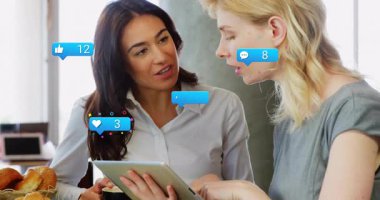 Tablette sosyal medya paylaşımı açan iki kadın, tepelerine tırmanan animasyon simgeleriyle verileri takip ediyorlar. İşbirliği, analitik, tartışma, dijital, modern, üretkenlik, sosyal