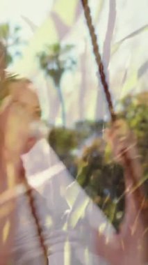 Elinde bir buket çiçek tutarken salıncakta sallanan bir gelinlik giyen beyaz bir gelinin dijital bileşimi. Çimenler arka planda hareket ediyor