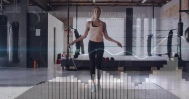 Kadın atlama halatını bacaklarının arkasında sallıyor ve spor salonunda dijital fitness ölçümlerini çalıştırıyor. Kardiyo, çeviklik, eğitim, atletizm, modern, enerjik, hareket