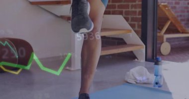 Adam sağ ayağını mindere kaldırıyor ve akıllı seğirmeleri kontrol ederken holografik fitness çizelgelerini aktifleştiriyor. Dayanıklılık eğitimi, dijital arayüz, giyilebilir teknoloji, spor salonu, spor izleme, spor kıyafeti, sağlık takibi.