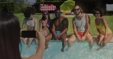 Havuz kenarında akıllı telefon çerçeveli bir kadın, yaşam tarzı fotoğrafçılığı için canlı poz veriyor. Açık hava, boş zaman, rahat, enerjik, dostluk, kutlama, yaz