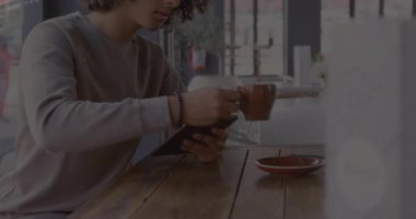 Adam kahve fincanını kaldırıyor ve tableti döndürüyor, siber tarama sonuçlarını şeffaf kaplamalarda gösteriyor. Teknoloji, siber güvenlik, veri analizi, modern çalışma alanı, dijital, ağ oluşturma, yenilik