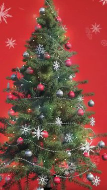 Kırmızı arka planda asılı duran süslemeler ve Noel ağacı üzerine düşen karların animasyonu. Noel şenliği ve kutlama konsepti
