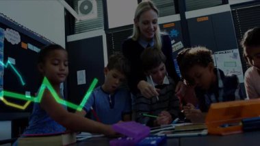 Ödevlerini yazan öğrencilere rehberlik eden öğretmen, yeşil-sarı grafiği masaya doğru süpürüyor. Eğitim, sınıf, işbirliği, öğrenme, akıl hocalığı, gençlik, akademik