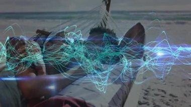 Hamakta dinlenen ve telefon uygulaması kullanan bir çift, plaj sahnesinde titreşen turkuaz dalga formu. Plaj, rahatlama, dijital, sükunet, doğa, rahatlık, refah