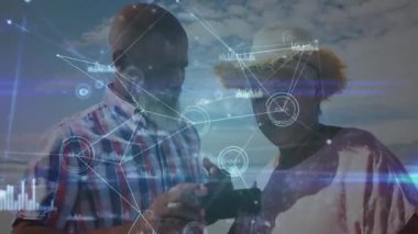 Kumsaldaki akıllı telefonu inceleyen çift dijital teknik grafikleri etkinleştiriyor sonra da eğlence olsun diye selfie çekiyor. Teknoloji, bağlantı, eğlence, açık hava, yaşam tarzı, yenilik, arkadaşlık