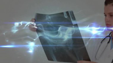 Röntgen filmi geliyor, kadın doktor film boyunca mavi çizgilerle dönen taramayı inceliyor. Tıbbi, sağlık, tanı, holografik, fütüristik, bilimsel, profesyonel