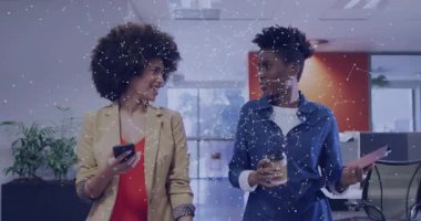 Ofiste yürürken gülümseyen, akıllı telefon gösteren, kahvelerini yudumlayan ve iş konuşan iki kadın. İşbirliği, takım çalışması, profesyonellik, modern, canlı, iletişim, işyeri