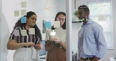 Proje ekibi tablet ekranı tıklatıyor ve iş planlama için cam bölme üzerine pasta grafiği çiziyor. İşbirliği, beyin fırtınası, yenilik, takım çalışması, sunum, strateji, danışma