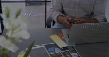 Tasarımcı çizelgelere uzanıyor sonra akıllı telefonu alıyor ve kahve içerken tasarımları gözden geçiriyor. Modern ofis, çalışma alanı, üretkenlik, teknoloji, yaratıcı profesyonel, dijital araçlar, iç tasarım