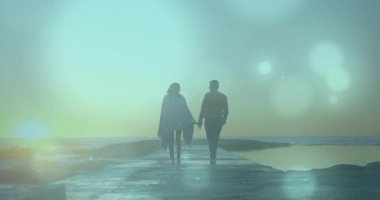 Gün doğumunda çift ellerini uzatıp yürüyen iskelede hareketli bokeh fişekleriyle seyahat ediyorlar. Romantizm, bağlantı, dinginlik, şafak, boş zaman, siluet, uyum.