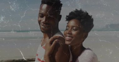 Kumsalda gezinen bir çift, seyahat klipsiyle, kadının erkeğin kollarını sarması, kameranın yakınlaşması. Romantik, şefkat, manzara, sükunet, bağlantı, boş zaman, yaşam tarzı