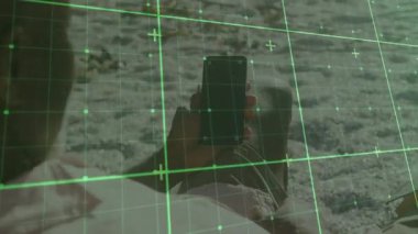 Kıyıya yaslanan adam akıllı telefonu ayarlıyor ve haritalandırma için dijital ızgara taraması başlatılıyor. Teknoloji, yenilik, fütüristik, açık hava, manzara, keşif, görselleştirme