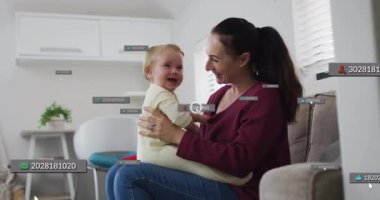 Baba kanepeye oturup bebeği kucağında tutuyor, gülümseyerek yüzen teknoloji ikonlarını aktifleştiriyor. Aile, ebeveynlik, şefkat, bağlılık, modern yaşam tarzı, dijital bağlantı, oyunculuk